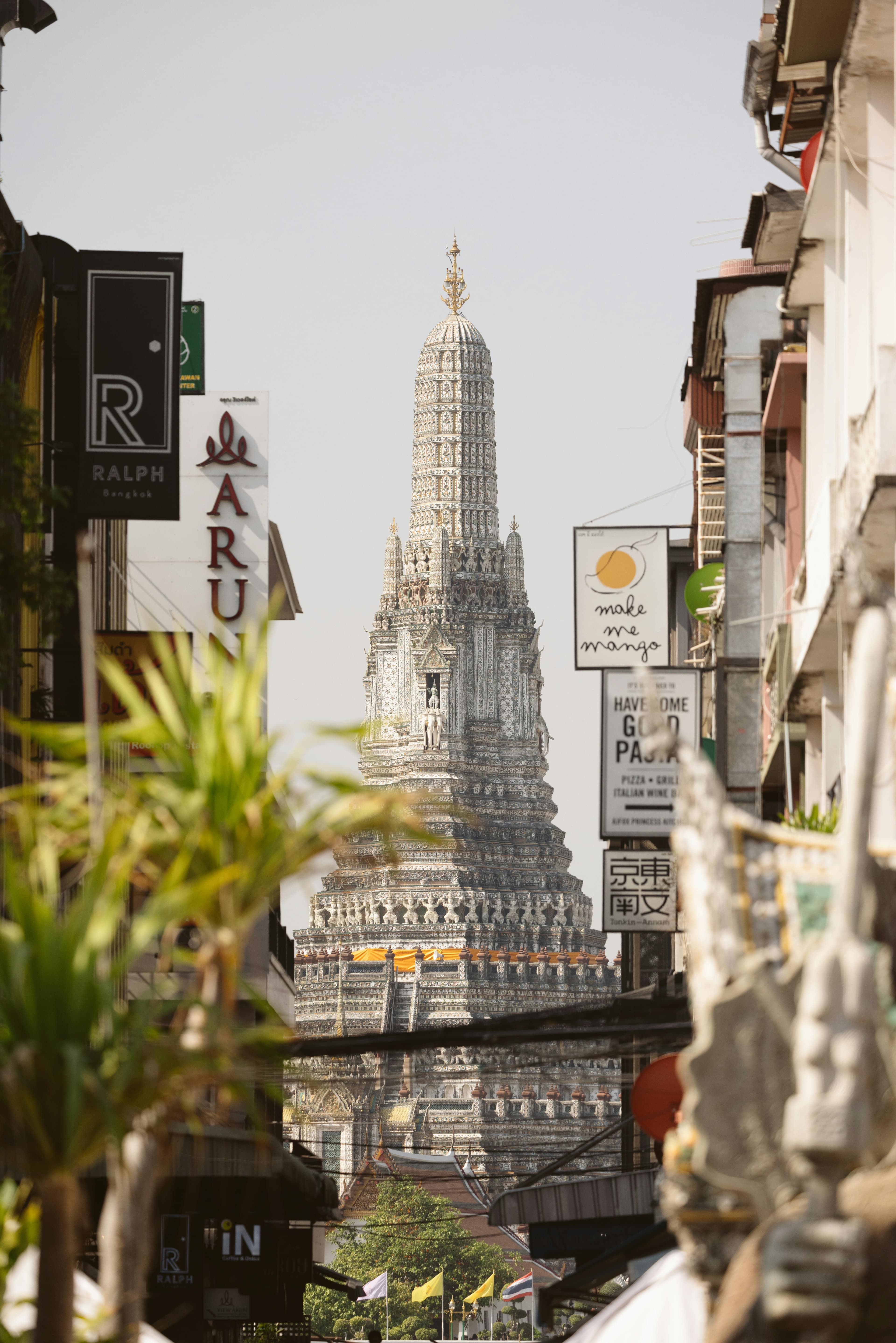 Wat Arun temple's central spire framed between Bangkok shop signs and streetlife.